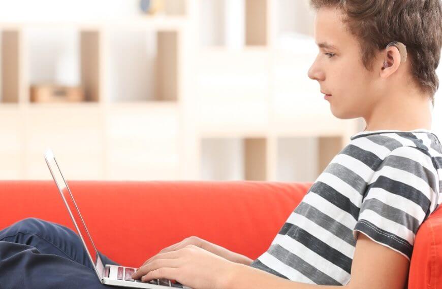 Picture this: A spirited and resilient young chap, engrossed in the magic of digital connectivity, stationed comfortably on a sofa. He navigates through the virtual maze with exceptional finesse, his laptop being his light and shield. Isn't technology amazing? It crafts bridges where once were walls for our hard of hearing youth. Let’s further foster those bridges, removing barriers and embracing inclusivity.