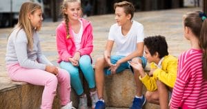 Five young minds, encapsulated by three vivacious girls and two energetic boys, are nestled comfortably on a sizeable stone structure, bathed in the tranquil ambiance of Mother Nature. Their faces are aglow - a stirring tableau of joy and genuine engagement underpinned by the rhythm of their lively chatter. They're not just exchanging words; they're building bridges of understanding, defying the silence that few can comprehend. Damn right - they’re hard of hearing but certainly not hard to inspire.