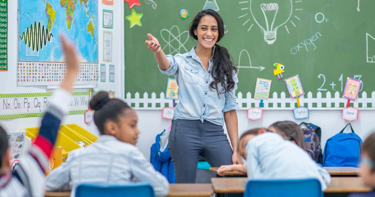 A smiling teacher engaging with students in a classroom, demonstrating the importance of clear communication for hard-of-hearing students using microphone systems.