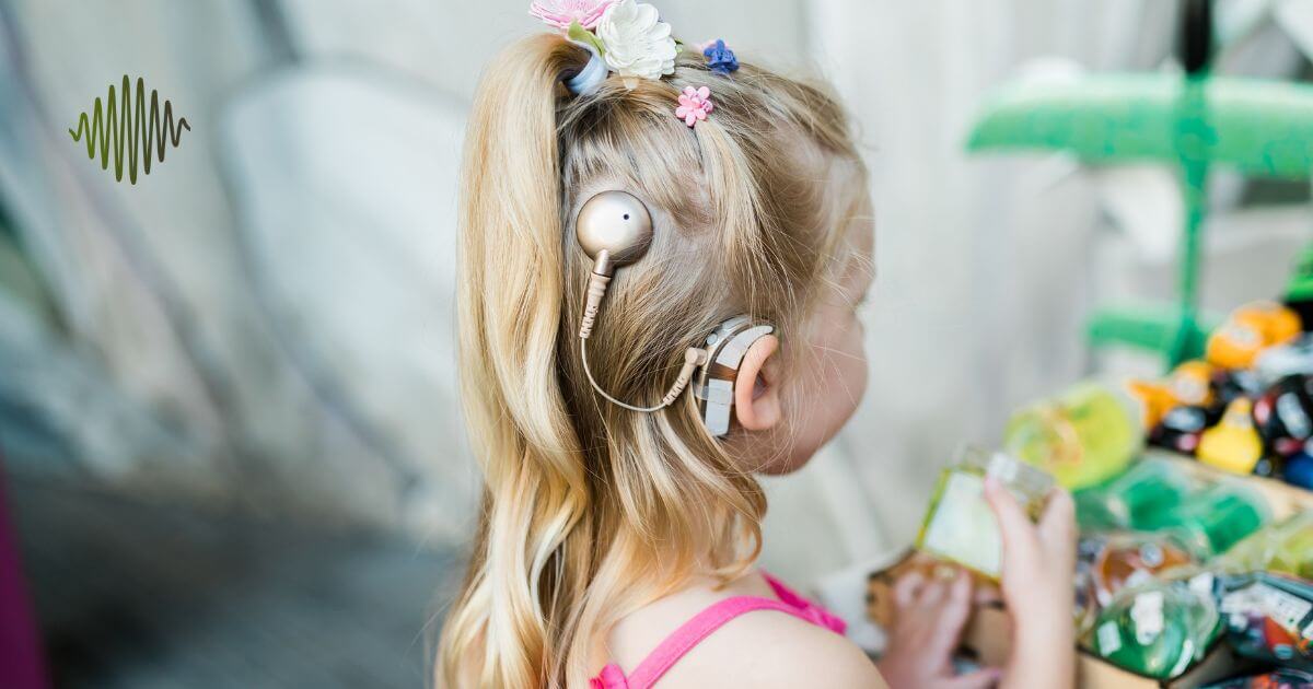 Picture this: A young girl with blonde hair, rocking a pink tank top, effortlessly flaunts an elegant cochlear implant accessory. This chic addition is just one of the "7 Cochlear Implant Accessories Every Parent Needs." While she eyes colorful snacks and trinkets, a vibrant green logo subtly adorns the upper corner. It's all about blending style with utility for our incredible hard of hearing youth!