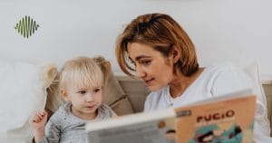 Imagine a cozy scene: a mother with chic short hair learened into a speech therapy book, sharing insights with her blonde, pigtailed daughter nestled on the bed. A signature green logo with wavy lines graces the top left corner, symbolizing our foundation’s dedication to empowering hard of hearing youth through engaging and supportive learning.