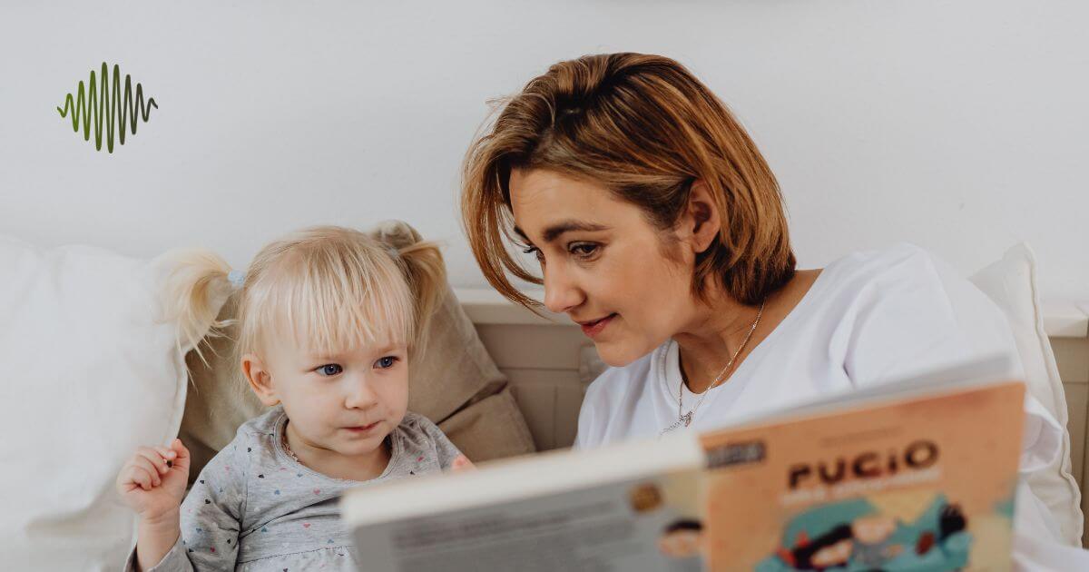 Imagine a cozy scene: a mother with chic short hair learened into a speech therapy book, sharing insights with her blonde, pigtailed daughter nestled on the bed. A signature green logo with wavy lines graces the top left corner, symbolizing our foundation’s dedication to empowering hard of hearing youth through engaging and supportive learning.